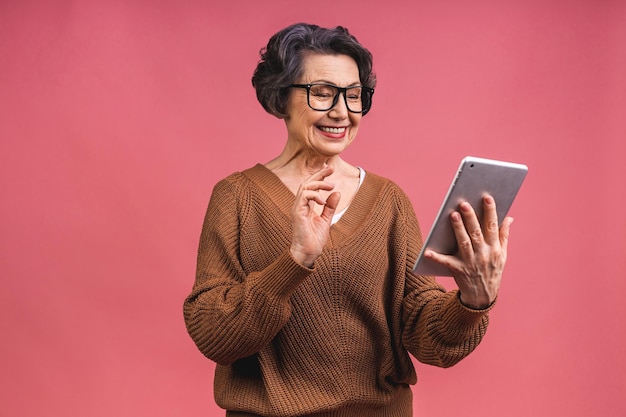 Foto ritratto di donna matura invecchiata maggiore con la nonna del computer della compressa isolata su fondo rosa