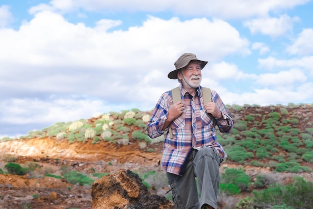 Portrait of a senior bearded man carrying a backpack looking at the mountain and smiling Fit old man on a hiking trip enjoying adventure freedom and healthy vacation