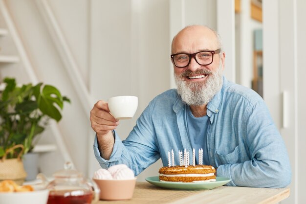 생일 케이크 차를 마시고 카메라에 미소와 함께 테이블에 앉아 안경에 수석 수염 난된 남자의 초상화