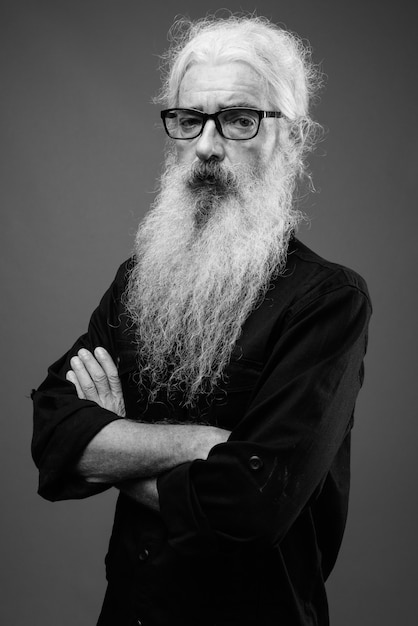 Portrait of senior bearded man wearing black shirt on gray in black and white