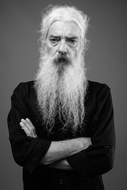 Portrait of senior bearded man wearing black shirt on gray in black and white