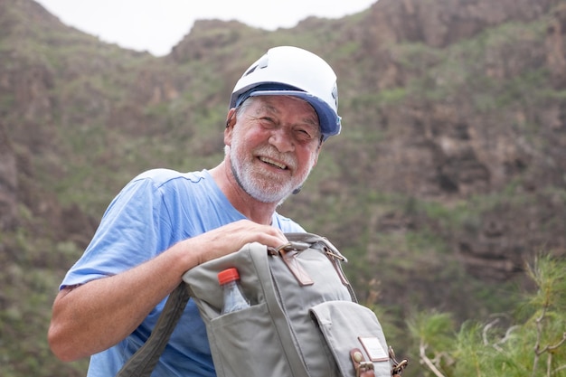 Portrait of Senior bearded man with helmet and backpack resting on the top of mountain in trekking