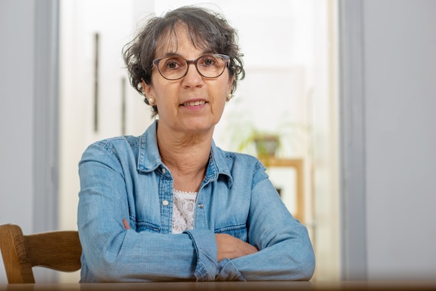 Portrait of senior brunette with  blue jeans jacket and glasses at home