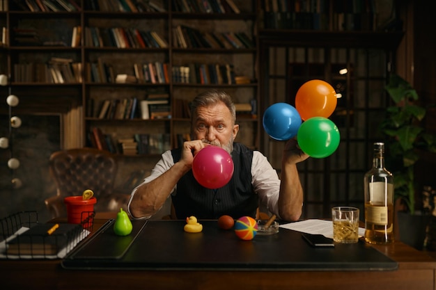 Portrait of senior business man blowing up balloon for success celebration