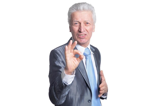 Portrait of senior businessman showing ok sign against white