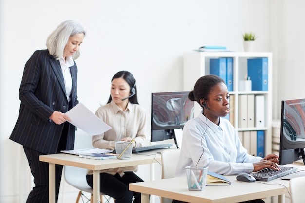 Portrait of senior businesswoman supervising call center operators in white office interior