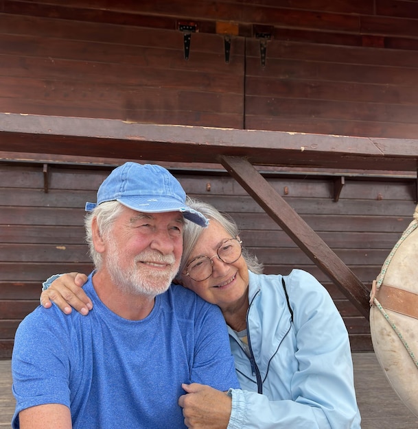 Portrait of senior caucasian couple exchange cuddles sitting together in outdoors enjoying vacation