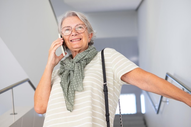 Portrait of senior Caucasian woman descending stairs inside building talking on cell phone