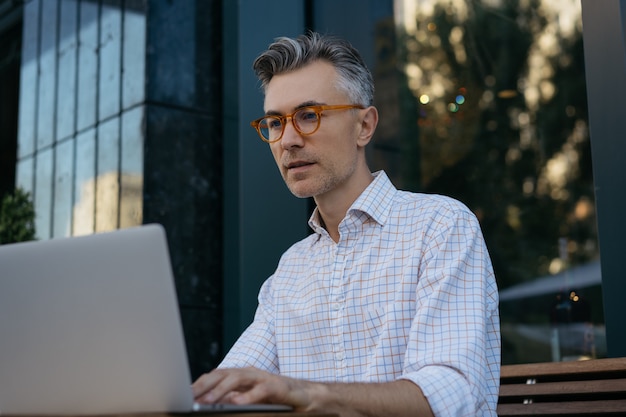 Portrait of senior developer using laptop , working outdoors