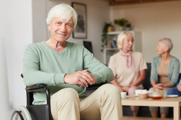 Portrait of senior disabled man smiling at camera with two women drinking tea