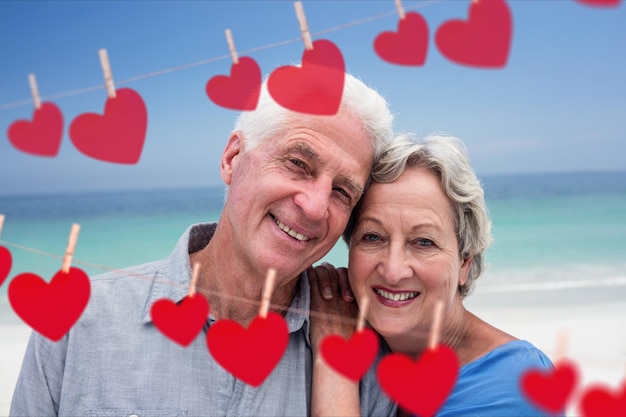 Portrait of senior embracing on beach against hearts hanging on a line