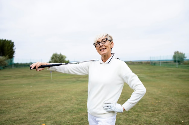 Portrait of senior female golfer with golf club standing on golf course.