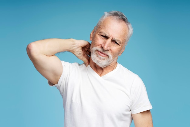 portrait of senior gray haired man looking away holding hand to neck pain injury