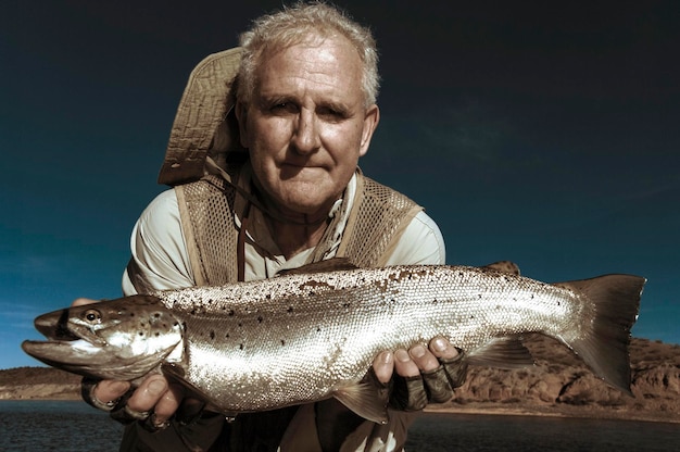 portrait of senior man holding fish while standing against blue sky