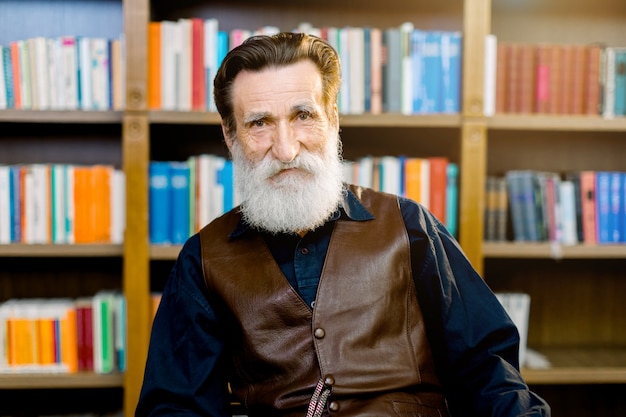 Портрет старшего человека, библиотекаря или академического профессора, сидя на фоне книжных шкафов и полок в библиотеке или на книжном магазине рынка. Счастливый книжный день мира, концепция библиотеки