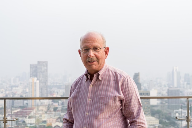 Portrait of senior man looking at camera in city at rooftop