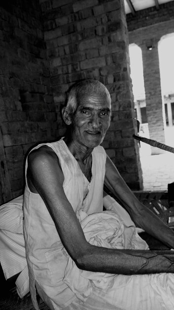 Photo portrait of senior man sitting on camp bed against wall