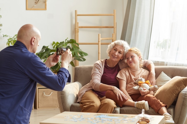 portrait of senior man taking smartphone photo of wife and granddaughter for family memories