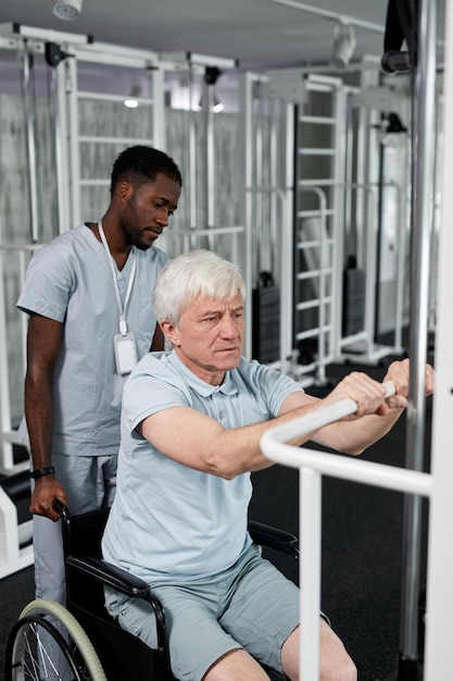 Portrait of senior man using wheelchair in gym and doing rehabilitation exercises