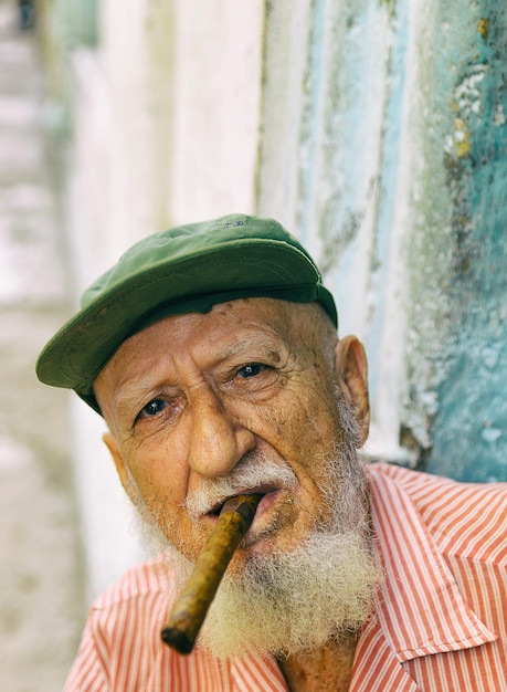 Foto ritratto di un uomo anziano che indossa un berretto e fuma un sigaro