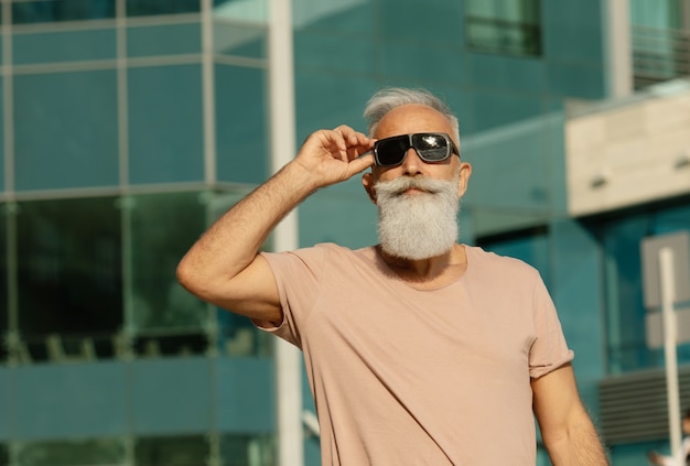 Ritratto di uomo anziano che indossa abiti casual che guarda lontano. uomo maturo con la barba che cammina per strada in una giornata estiva.
