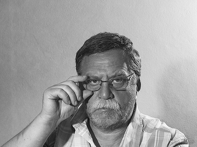 Photo portrait of senior man wearing eyeglasses while sitting against wall at home