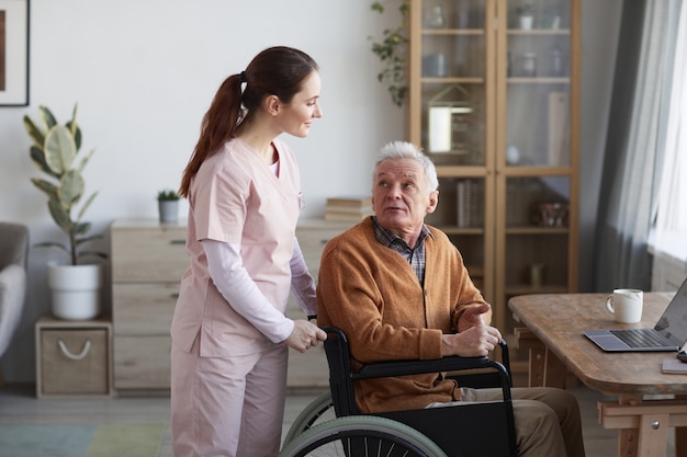 Portrait of senior man in wheelchair looking at caregiver helping him, copy space