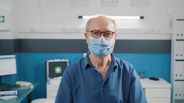 Portrait of senior man with face mask attending recovery\
examination with doctor. patient in retirement age waiting on medic\
to do health care consultation in medical cabinet. physical\
exam.