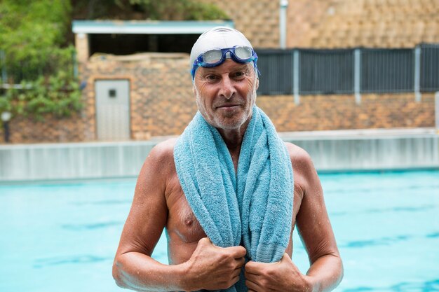 Portrait of senior man with towel over his shoulders standing at poolside