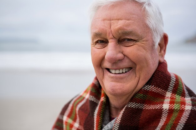 Portrait of senior man wrapped in shawl on beach