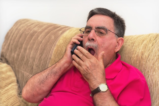 Ritratto di un uomo anziano sbadigliando, parlando al telefono. conversazione noiosa.