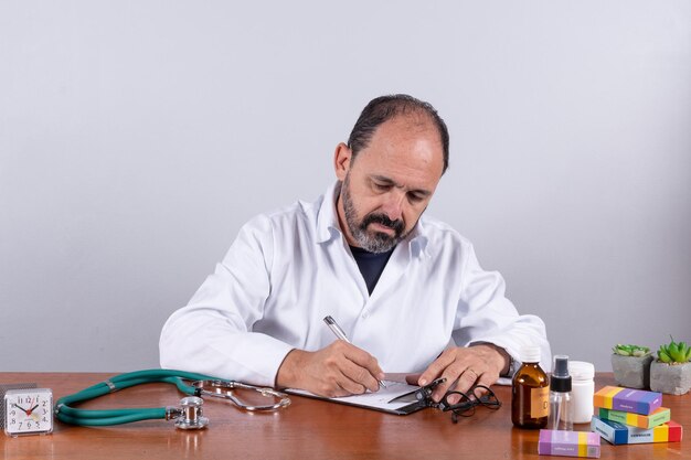 Portrait of senior mature doctor pleasant professional in white coat sitting at table