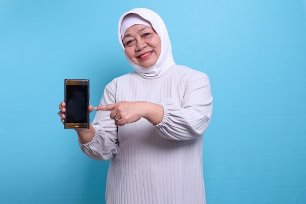 Portrait of a senior muslim woman smiling holding smartphone and pointing finger at the blank phone