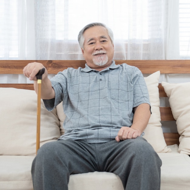 수석 노인 아시아 남자의 초상화 코치 손을 잡고 지팡이 지팡이 행복과 건강 한 라이프 스타일을 가진 집에서 소파에 앉아 도움이 앉아.