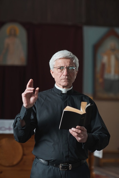 Foto ritratto di un sacerdote anziano che legge la bibbia durante una messa in chiesa