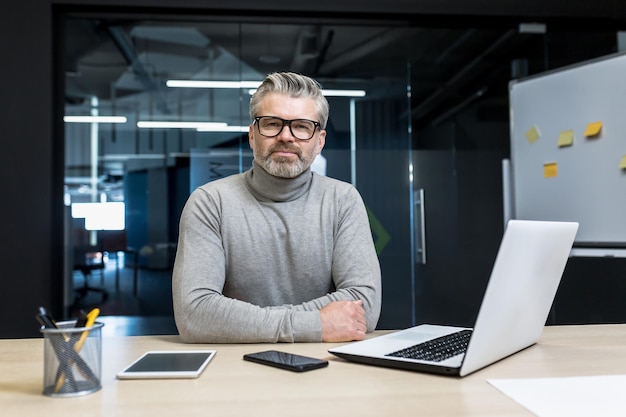 Ritratto del capo della squadra maturo del programmatore senior serio e concentrato che esamina l'uomo d'affari della macchina fotografica