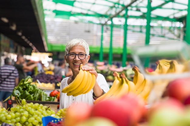 Portrait of senior woman buys bananas at the market