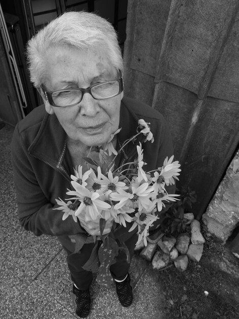 Photo portrait of senior woman holding flowers on sidewalk
