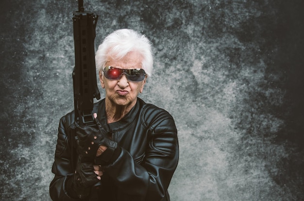 Photo portrait of senior woman holding rifle against wall