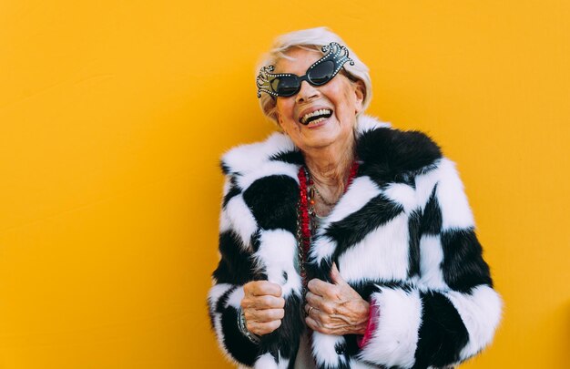 Photo portrait of senior woman laughing while standing against yellow background