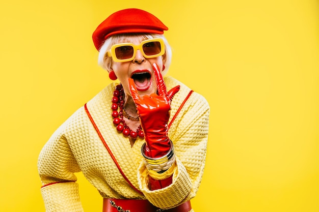 Photo portrait of senior woman wearing hat gesturing against yellow background