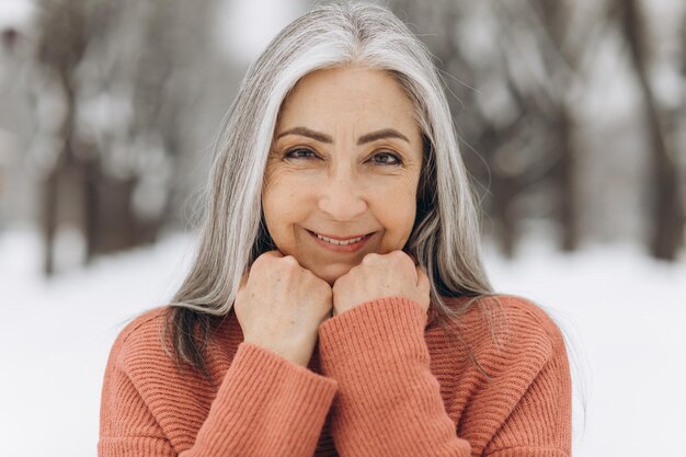 Ritratto di donna anziana con capelli grigi in maglione lavorato a maglia sorridente su sfondo di neve in inverno