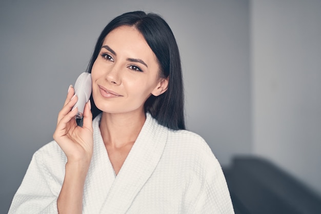 Portrait of a serene young woman with a facial cleansing massager looking into the distance