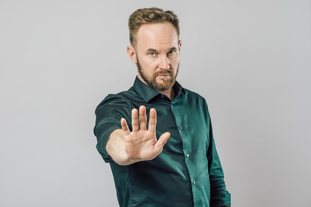 Portrait of a serious bearded man showing stop gesture with his palm isolated over gray background