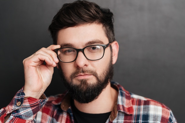 Portrait of serious bearded man touching glasses standing on chalkboard.