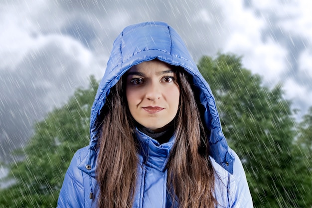 Foto ritratto di una bella ragazza seria che indossa un impermeabile blu con cappuccio in una giornata piovosa