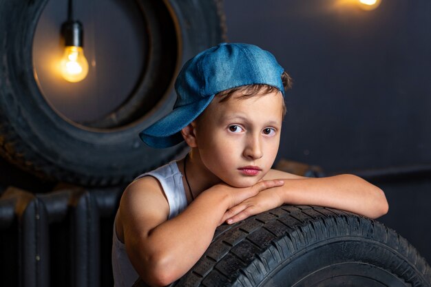 Portrait serious boy of 7 years old, ileaning on the tire of a car in garage