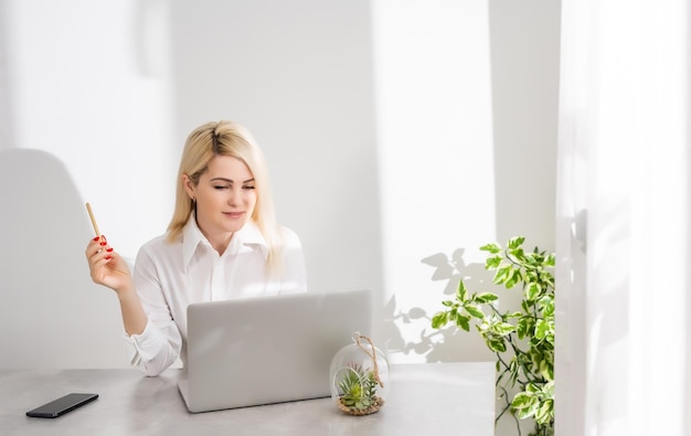 Portrait of a serious businesswoman using laptop in office against a white wall