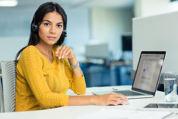 Photo portrait of a serious casual businesswoman sitting at the table with laptop in office