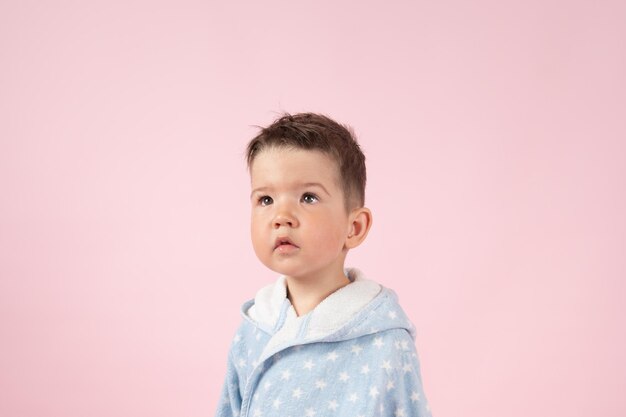 Portrait of serious caucasian kid boy in bathrobe on pink background High quality photo